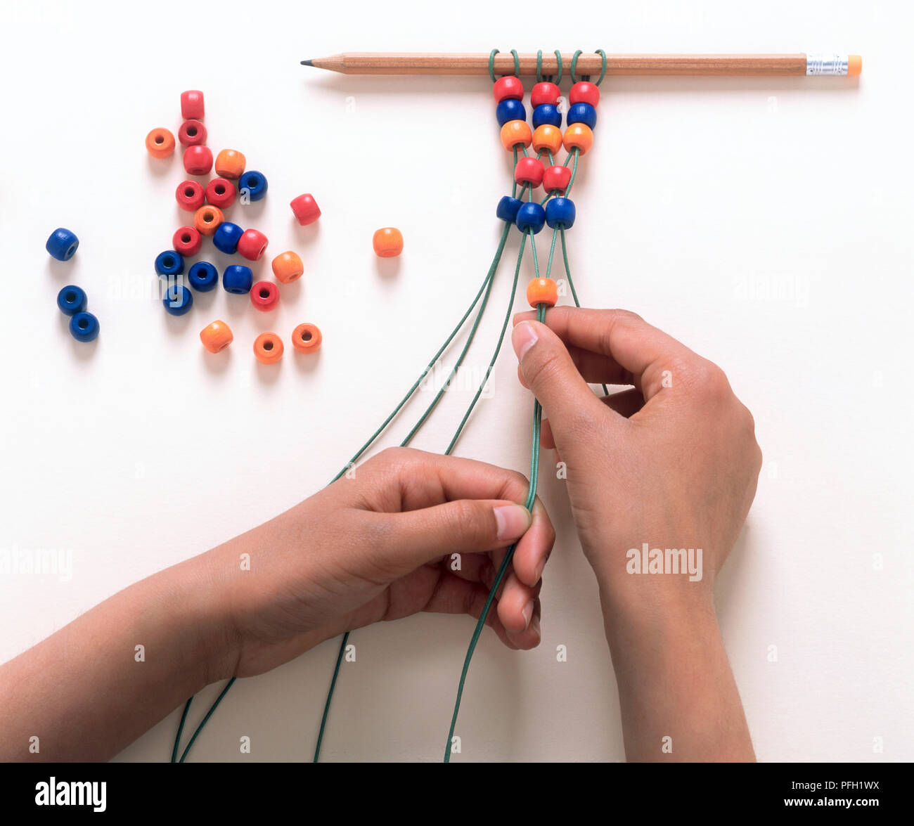 Perle di threading sulla stringa avvolta ad anello attorno ad una matita (rendendo la collana) Foto Stock