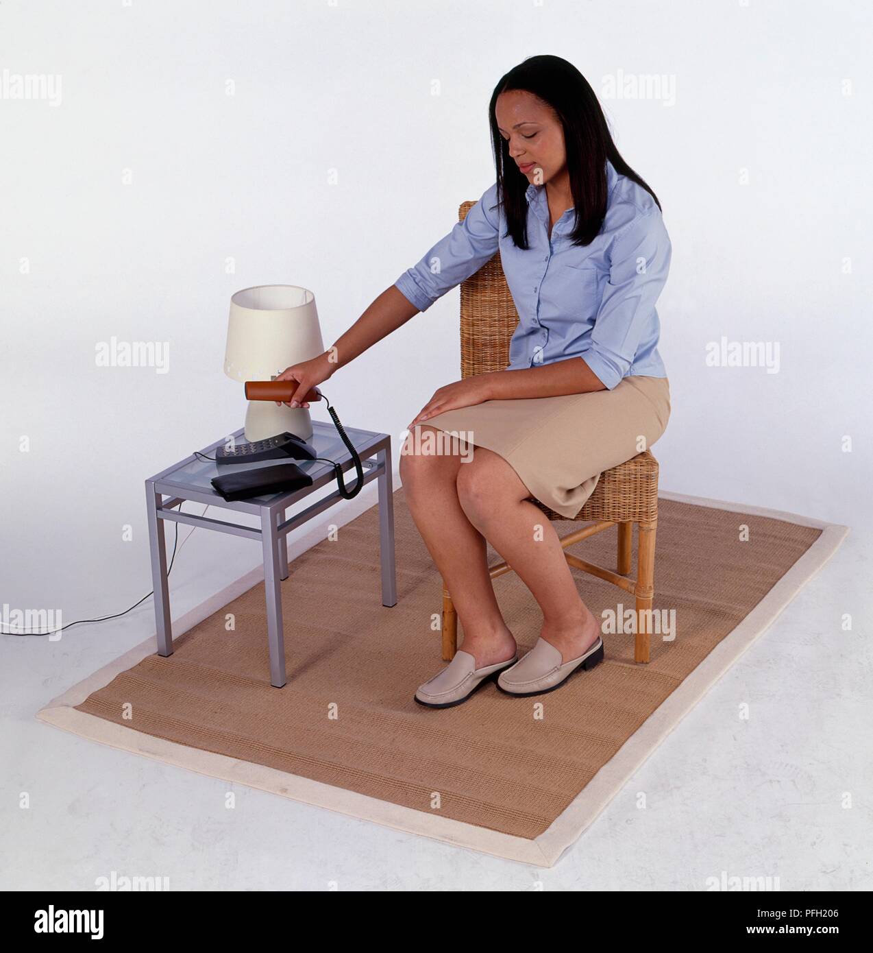Donna seduto su una sedia di mettere il ricevitore torna verso il telefono cellulare Foto Stock