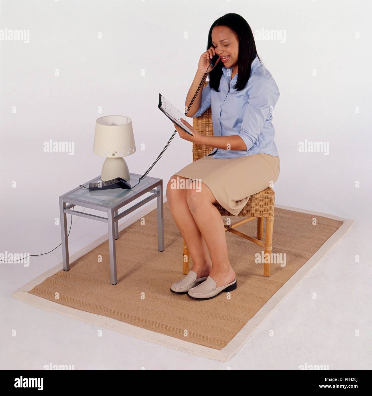 Donna seduto su una sedia di parlare al telefono tenendo diario Foto Stock
