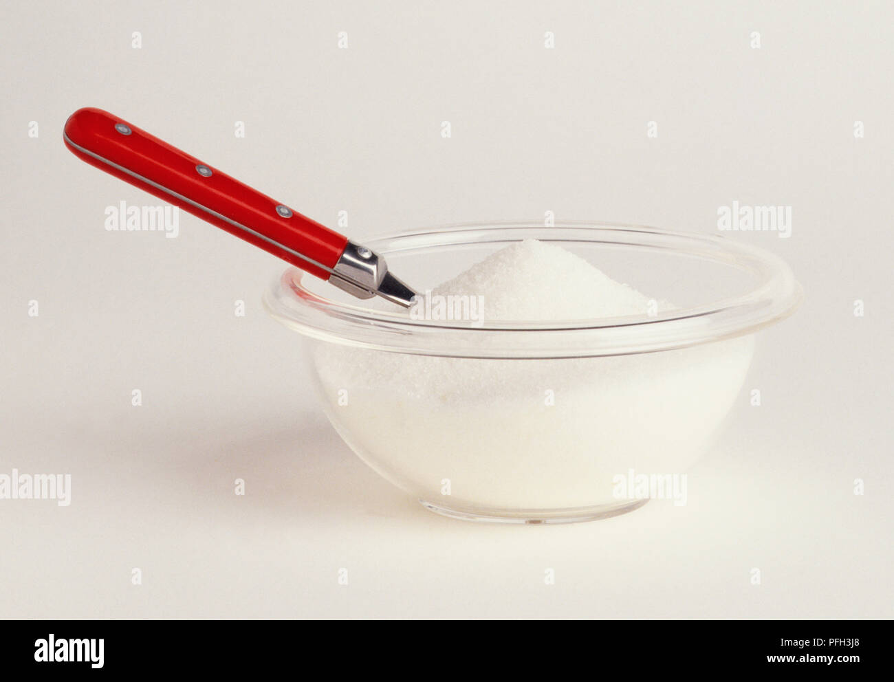 Cucchiaio con manico rosso incorporato in una ciotola di zucchero, vista laterale Foto Stock