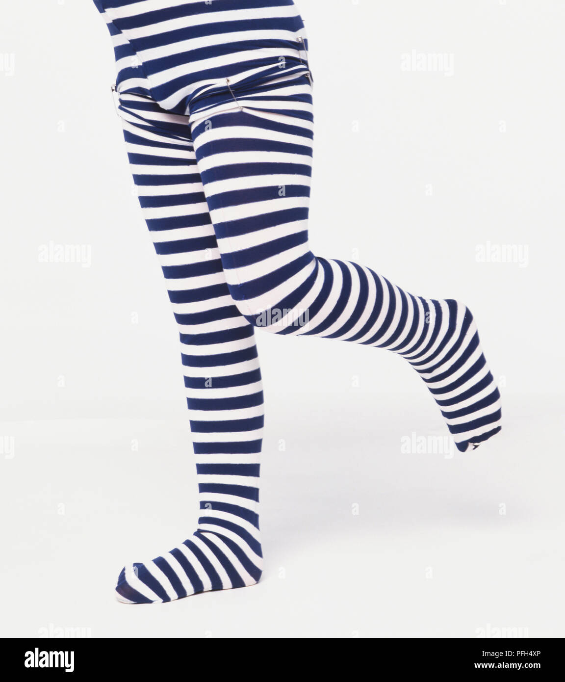 Bambino che indossa un blu e bianca a strisce costume in piedi su una gamba sola, alla cintura verso il basso Foto Stock