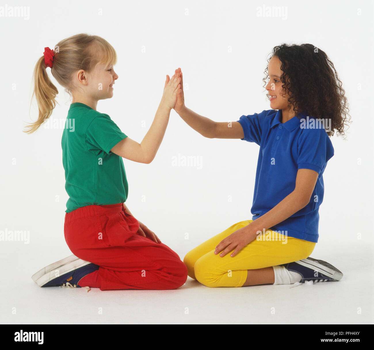 Due ragazze in abiti colorati seduto sulle ginocchia e battimani reciprocamente le mani Foto Stock
