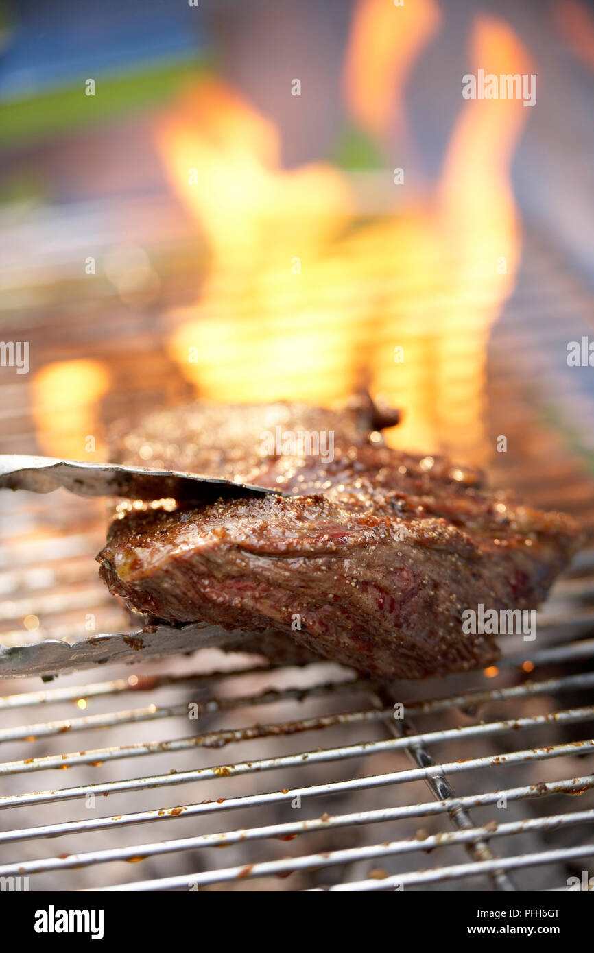 Pepe-incrostato bistecca di fianco sul barbecue grill, tenaglie Foto Stock