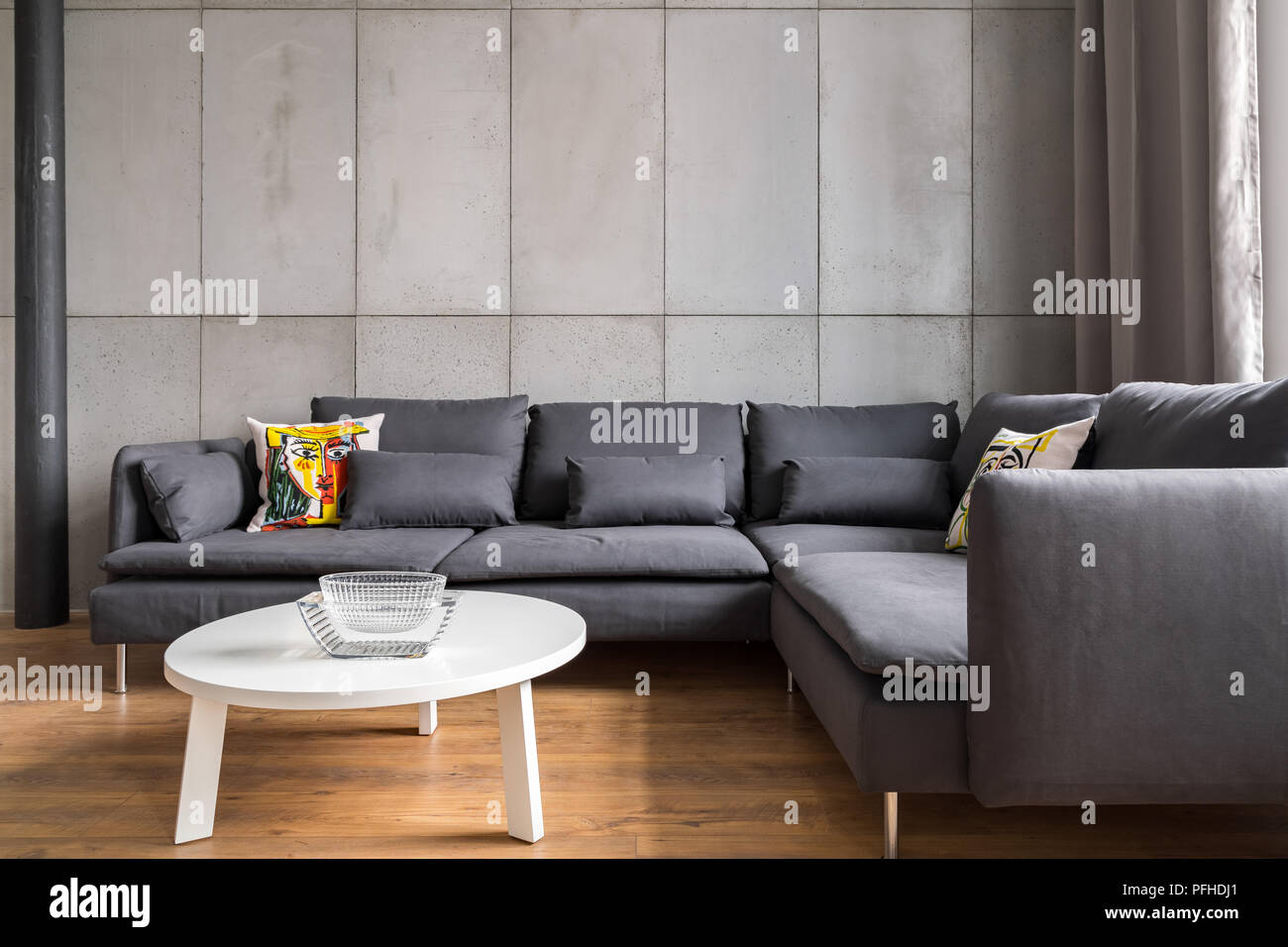 Arredamento moderno con parete in cemento, grande angolo divano e tavolo bianco Foto Stock