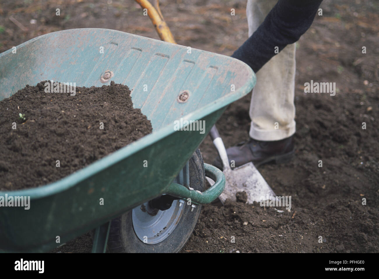 Topsoil in una ruota di Barrow, uomo scava in terreno dietro Foto Stock