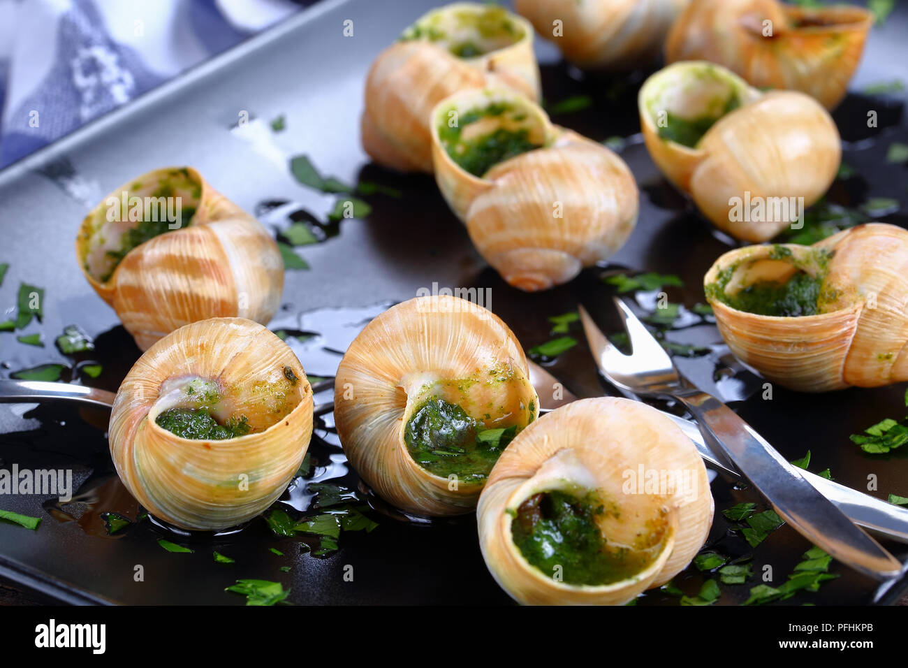 Delizioso piatto gourmet - Escargots de Bourgogne o lumache con burro alle erbe aglio spruzzata con del prezzemolo tritato finemente sulla piastra nera con lumaca per Foto Stock