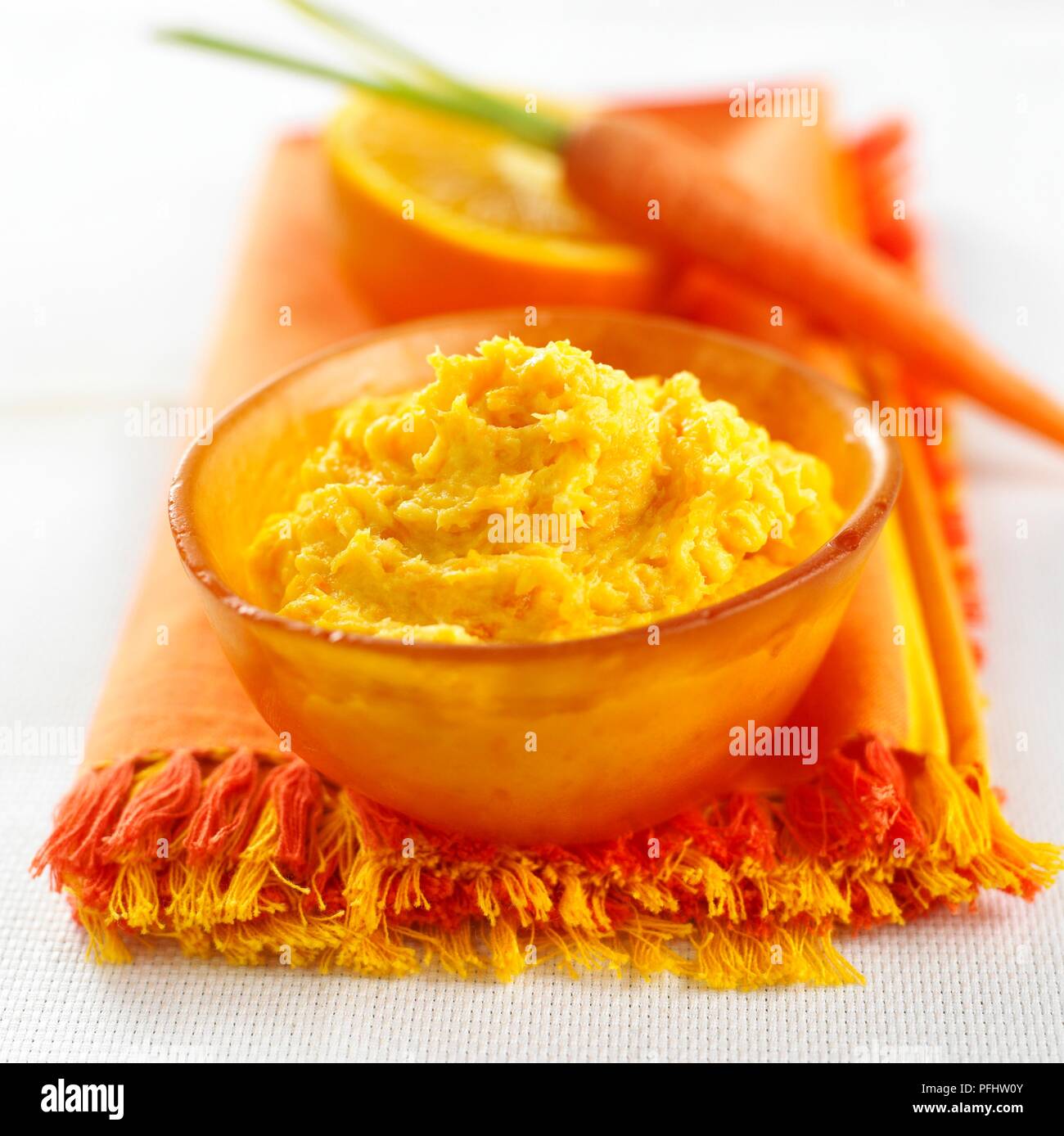 Ciotola di carota e purea di arancia sul tovagliolo arancio, carota fresca e orange in background Foto Stock