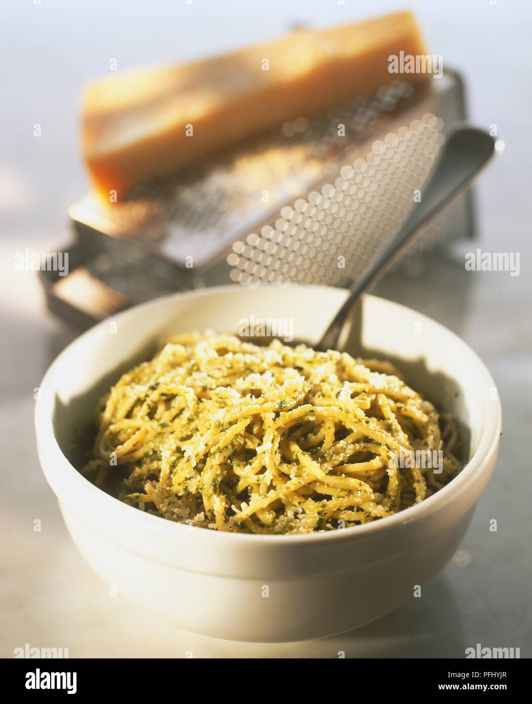Ciotola di spaghetti al pesto cosparso con formaggio grattugiato, blocco di formaggio sulla grattugia in background, vicino. Foto Stock