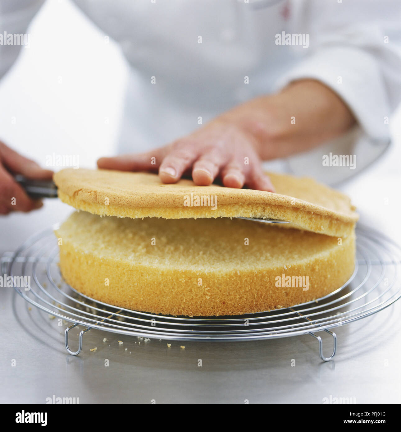 Affettare la parte superiore di un pan di Spagna rotondo in appoggio su un filo rack Foto Stock