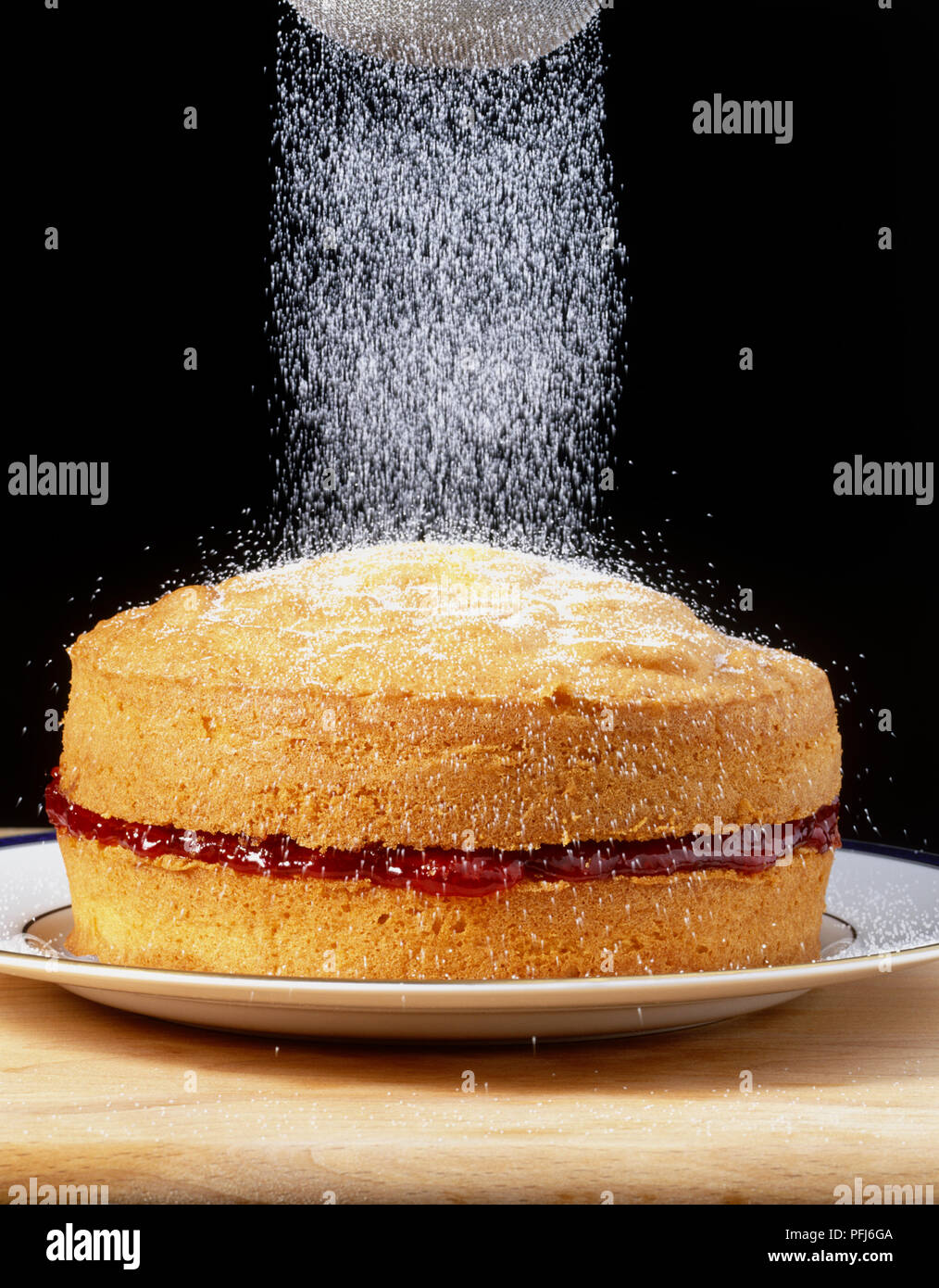 Jam-riempito Victoria sponge cake essendo spolverati con zucchero, vista laterale. Foto Stock