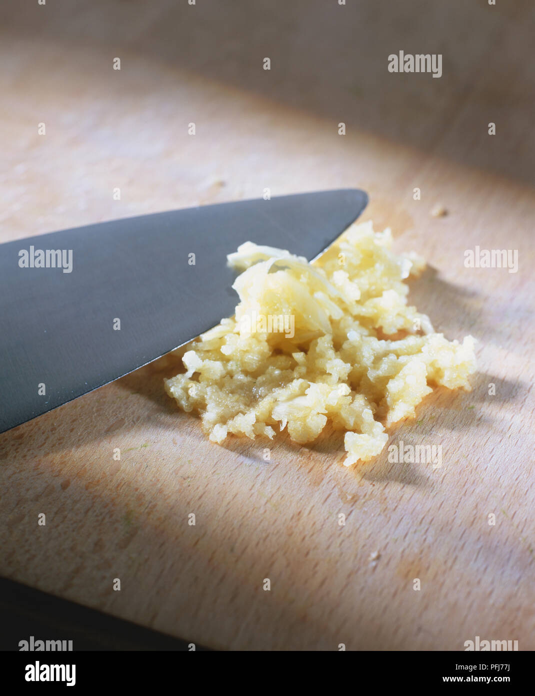 Allium sativum, aglio tritato finemente con grande coltello, sul tagliere di legno. Foto Stock