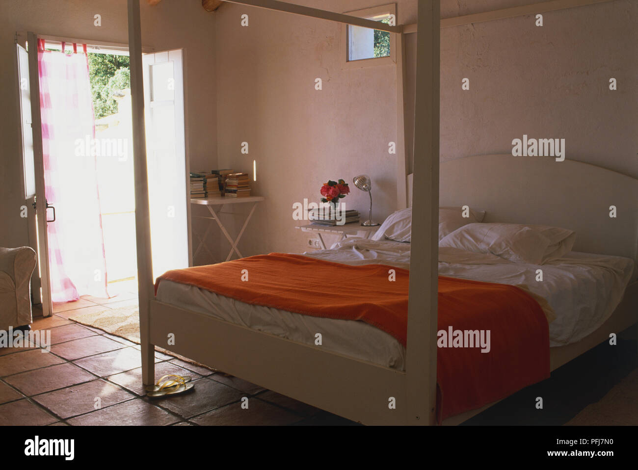 Camera da letto con pareti dipinte di bianco, bianco letto a baldacchino, lino bianco, arancio brillante cotone drappeggiato passi attraverso Foto Stock