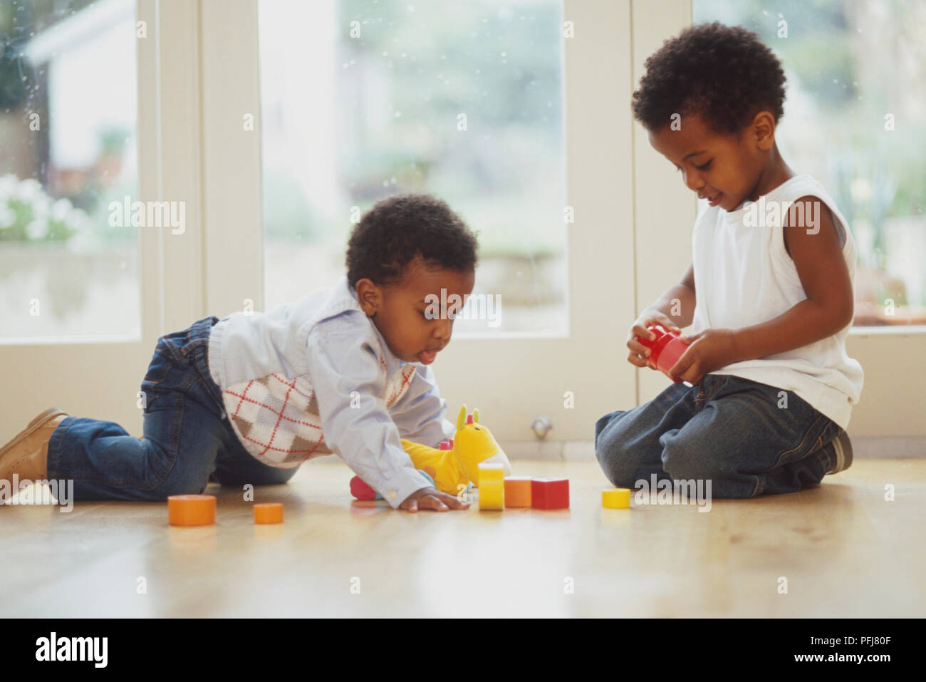 Due bambini seduti sul pavimento in legno nella parte anteriore della porta di patio giocando con il giocattolo morbido e cubi Foto Stock