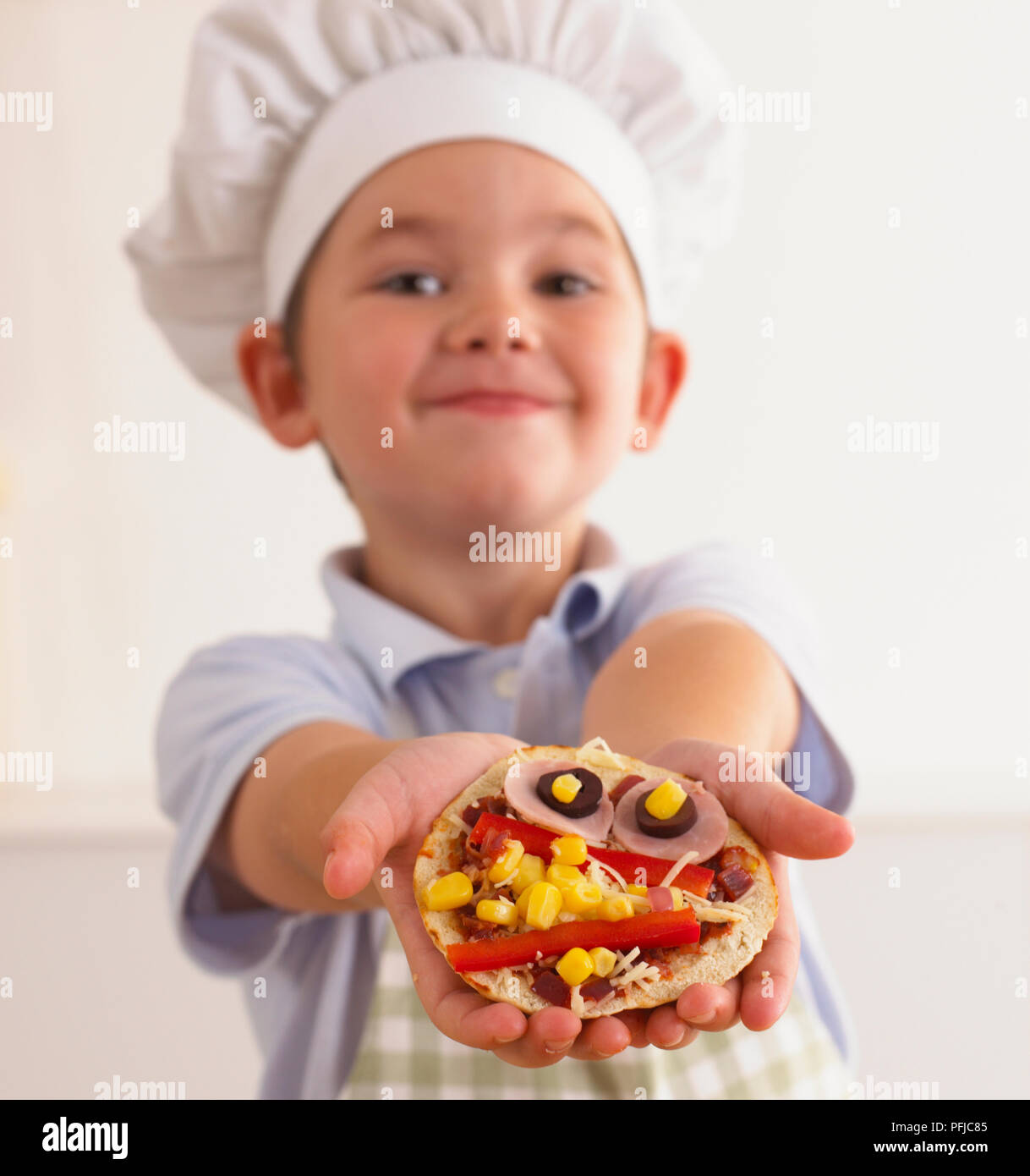 Ragazzo in chef hat mostra crudo pizza pitta, close-up Foto Stock