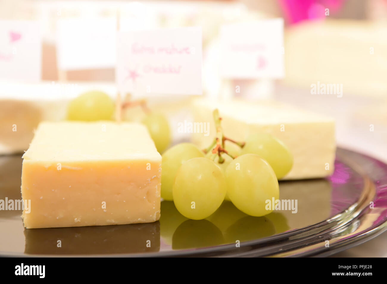 Formaggio e uva con etichette su una piastra nera con fuori fuoco sfondo Foto Stock