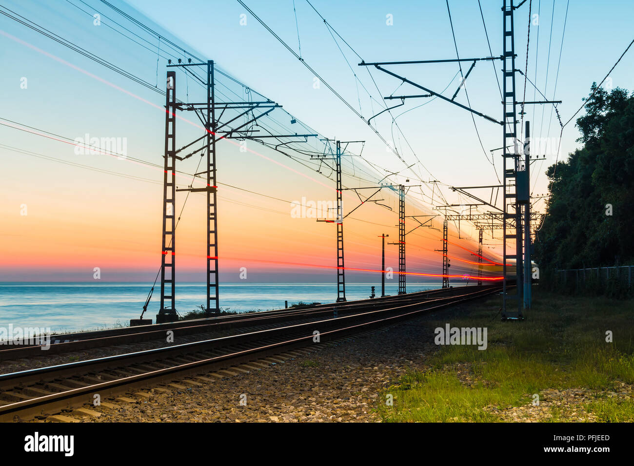 Lo splendido paesaggio di una ferrovia con moto treno sfocata sullo sfondo del mare al crepuscolo, Sochi, Russia Foto Stock