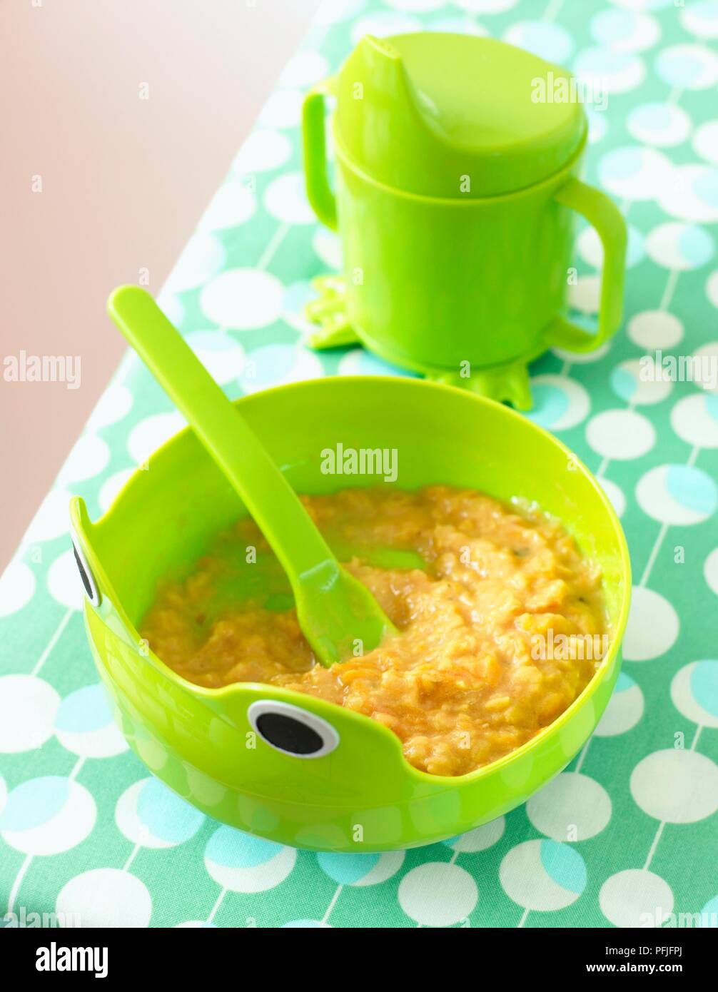 Lenticchia e purea di carota in verde ciotola con cucchiaio incorporato, e tazza verde con beccuccio Foto Stock
