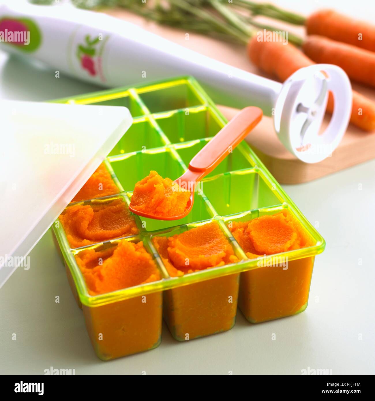 Porzioni di purea di carota congelati in un vassoio di plastica, frullatore a immersione e le carote fresche nelle vicinanze, close-up Foto Stock