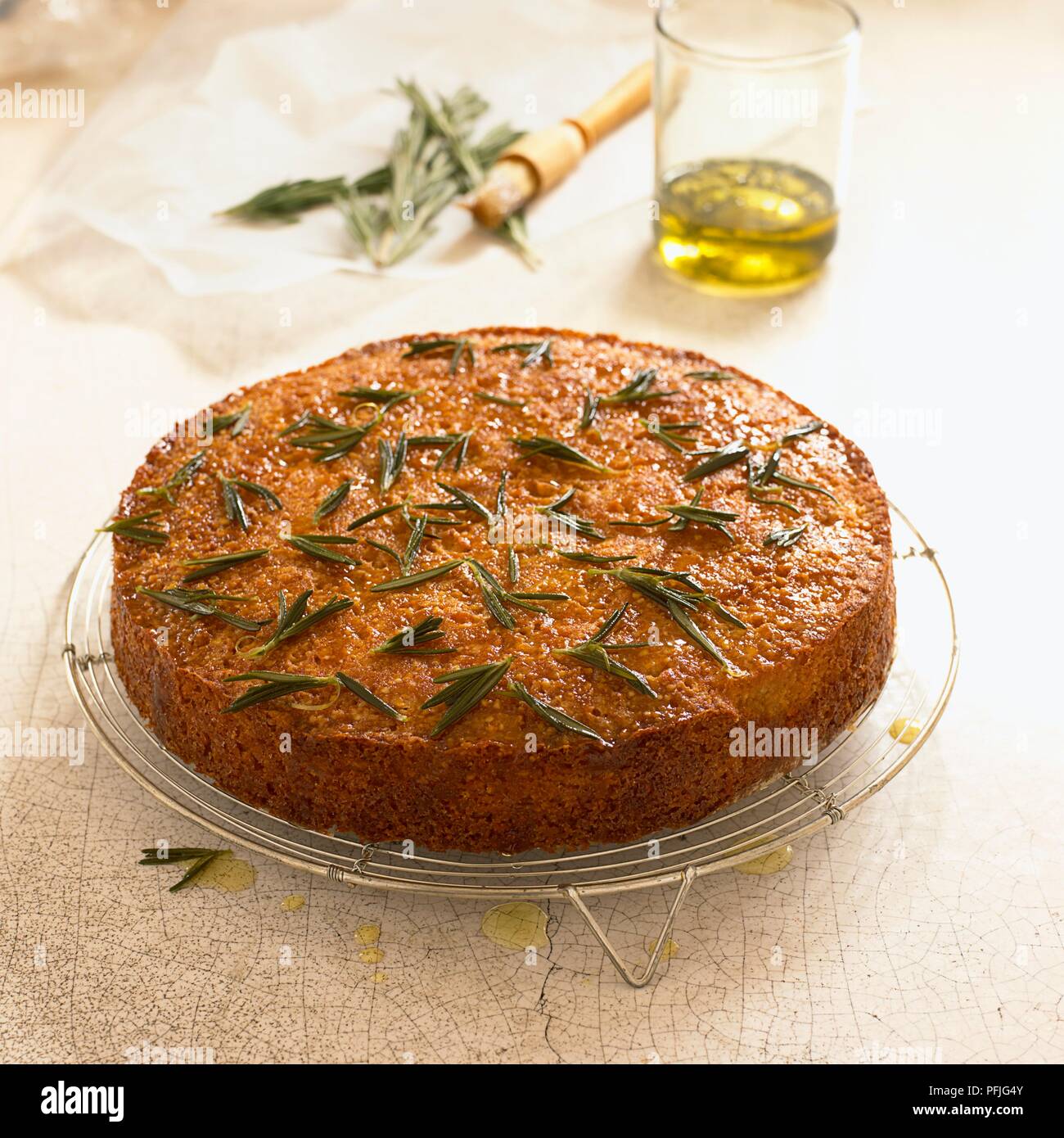Torta di polenta e rosmarino, con un bicchiere di olio di oliva, pasticceria pennello e rametti di rosmarino nelle vicinanze Foto Stock