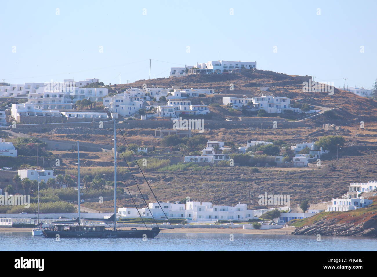 Nave sulla spiaggia con case bianche punteggiando una collina dell'isola greca di Mykonos Foto Stock