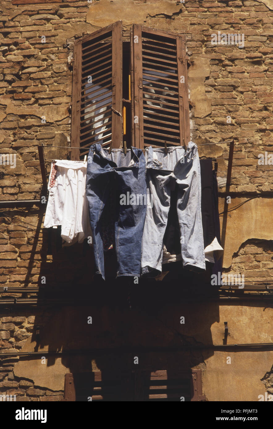 L'Italia, la Toscana centrale, Siena, lavaggio appeso dalle linee al di fuori di finestra con persiane di legno e a basso angolo di visione Foto Stock