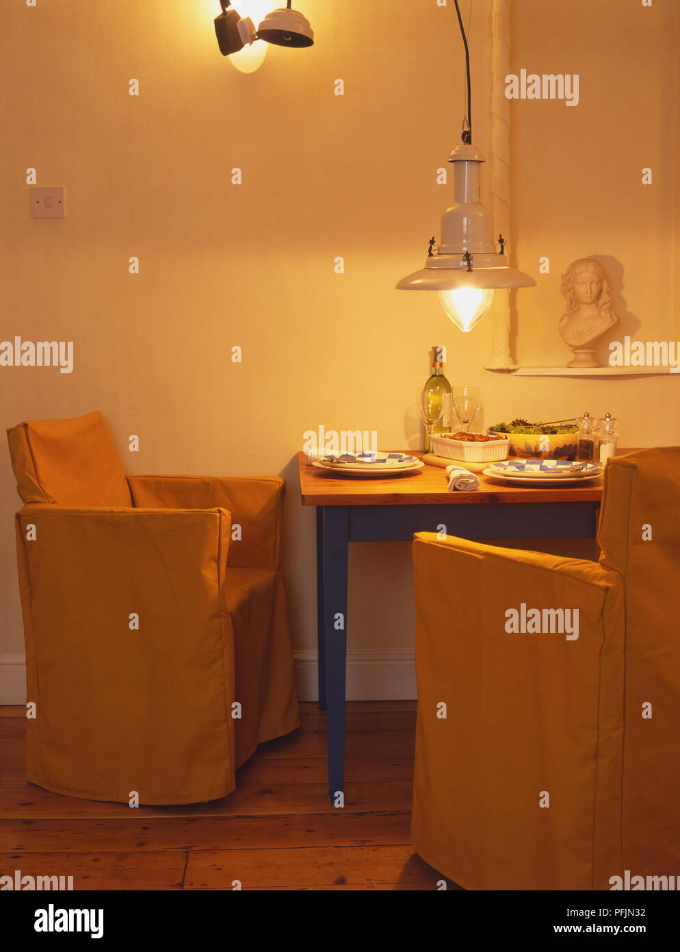 Tavolino in piedi contro la parete stabilite per la cena per due, due poltrone di colore giallo, bassa lampadario, vista laterale. Foto Stock