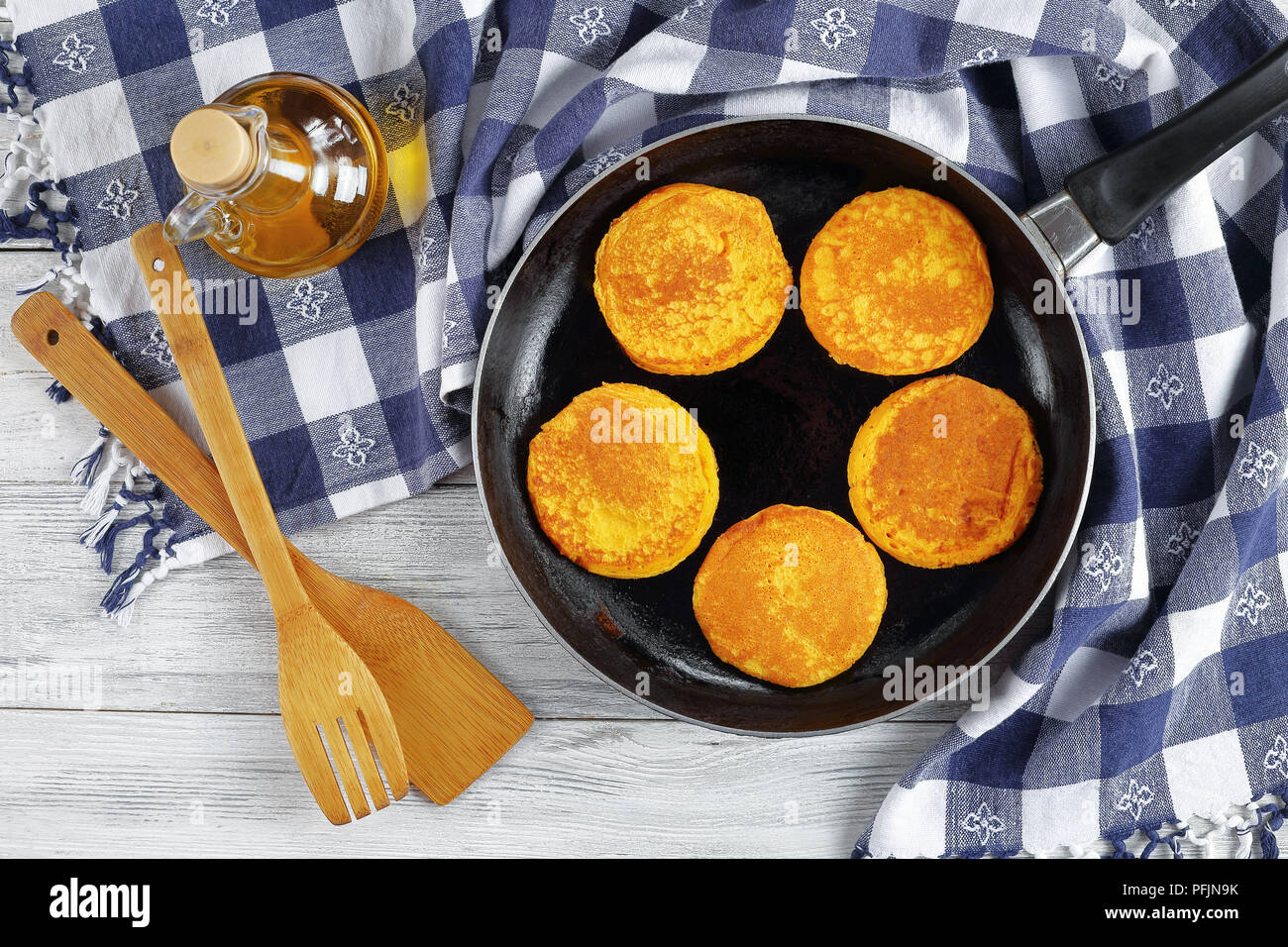 Delizioso giallo oro Frittelle di zucca in padella sul tavolo di legno con carta asciugatutto, spatole di legno e una bottiglia di olio di oliva, vista da sopra Foto Stock