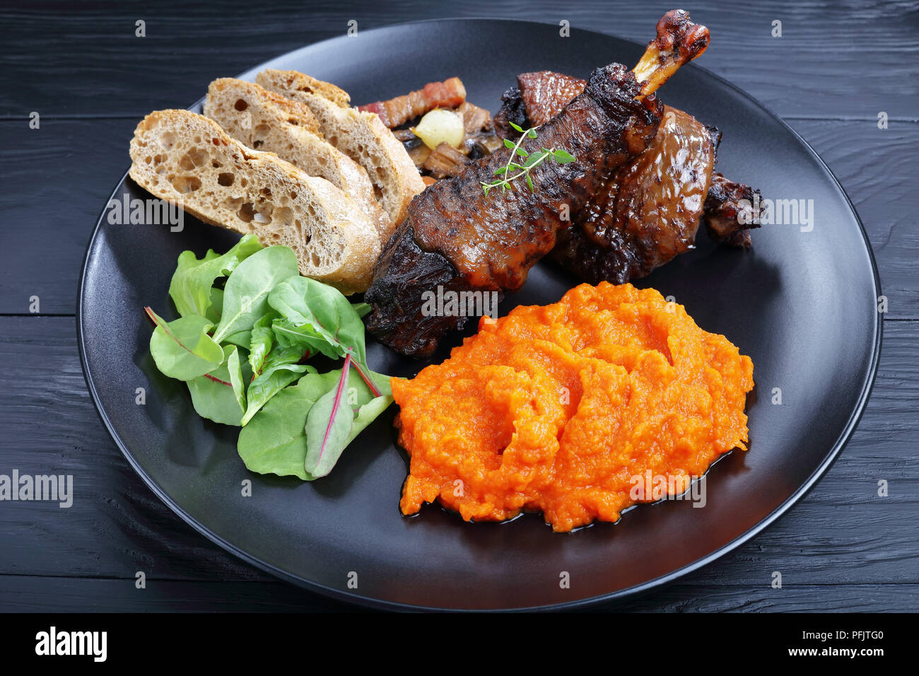 Una porzione di Coq au Vin - classica francese spezzatino di pollo servito sulla piastra nera con un mix di foglie di lattuga e purea di zucca, orizzontale vista da sopra Foto Stock