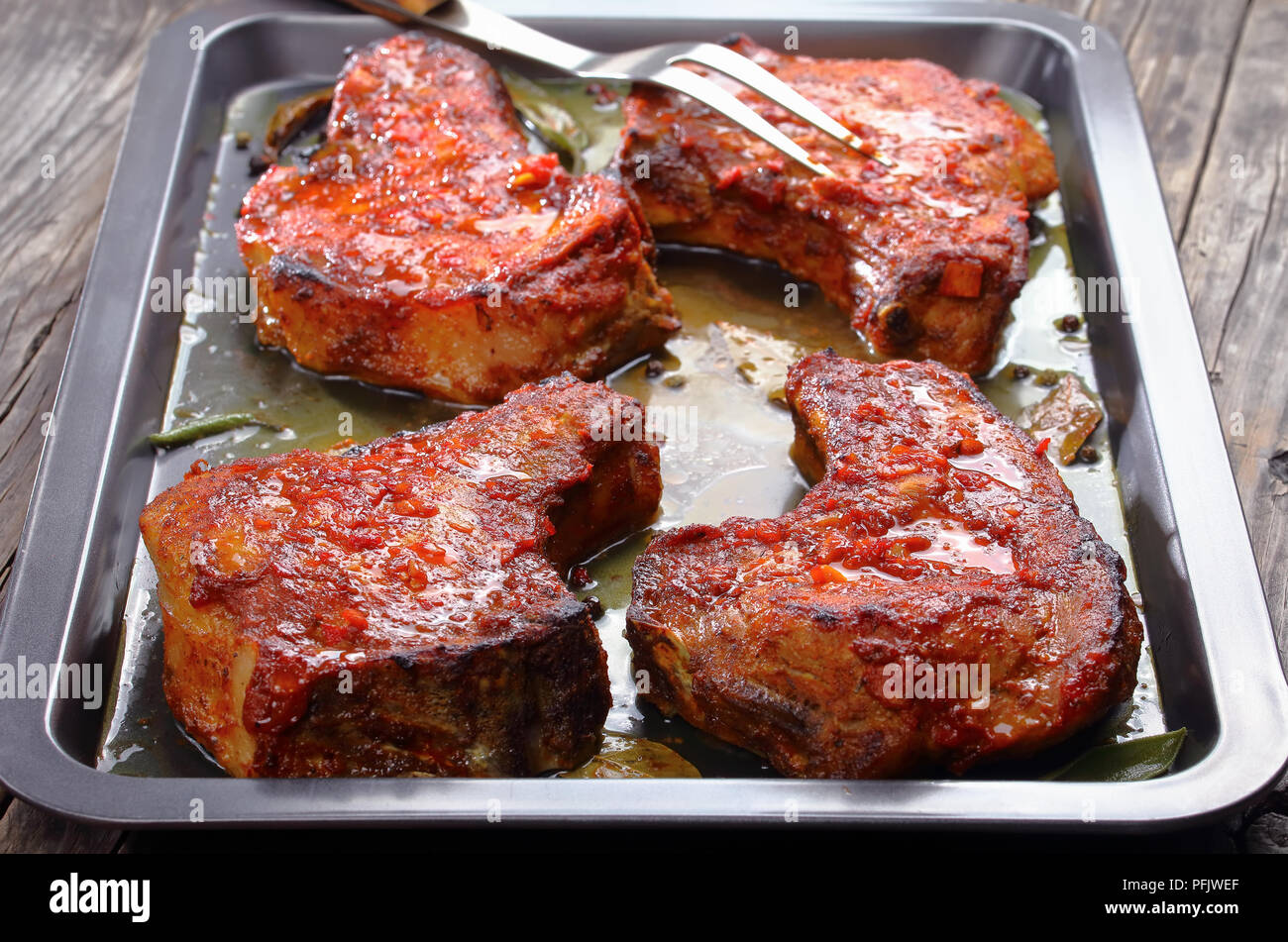 Arrosto di tenera, succulenta costolette di maiale sulla teglia con foglie di alloro e spezie e forcella per carne, facile ricetta per la cena di Natale, vista laterale dall'alto, Foto Stock