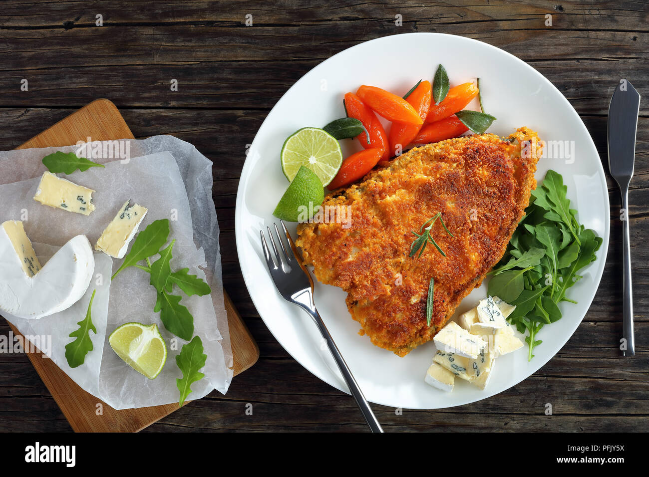 Deliziosa panate bianco bistecca di pesce serviti su piastra bianca con carote glassate, fresche fettine di lime, Formaggi a Muffa Blu e insalata di rucola, ingredienti Foto Stock