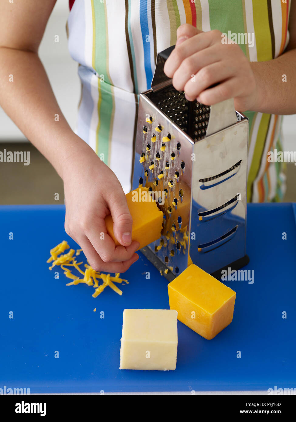 La mano della bambina grattugiare il formaggio sul tagliere, close-up Foto Stock