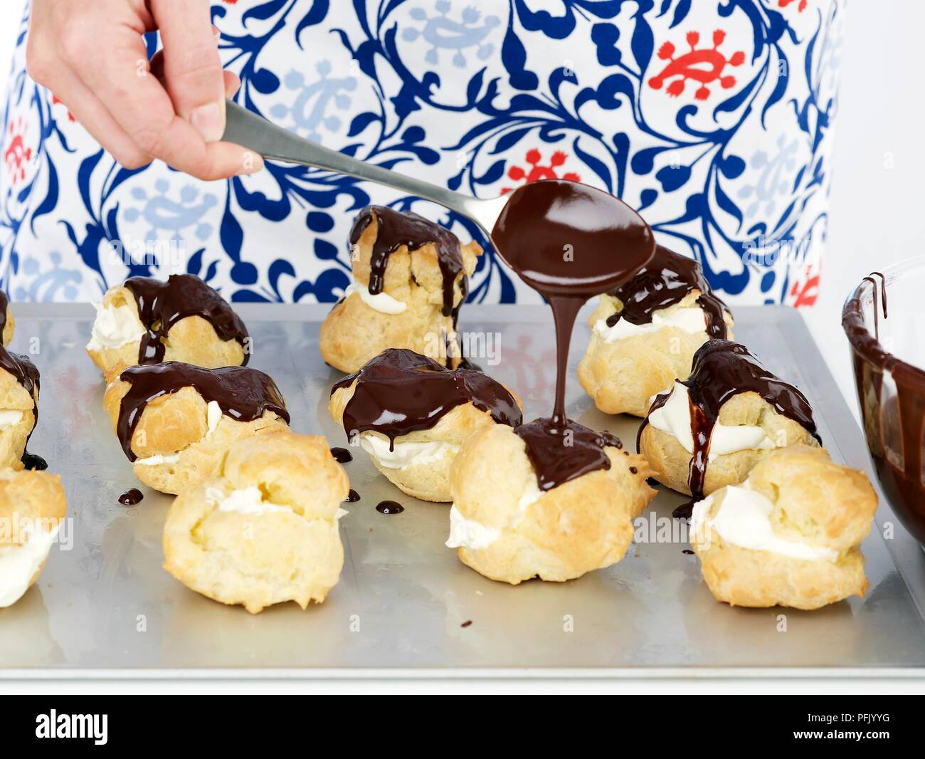 Versare il cioccolato su profiteroles sul vassoio da forno con cucchiaio, close-up Foto Stock