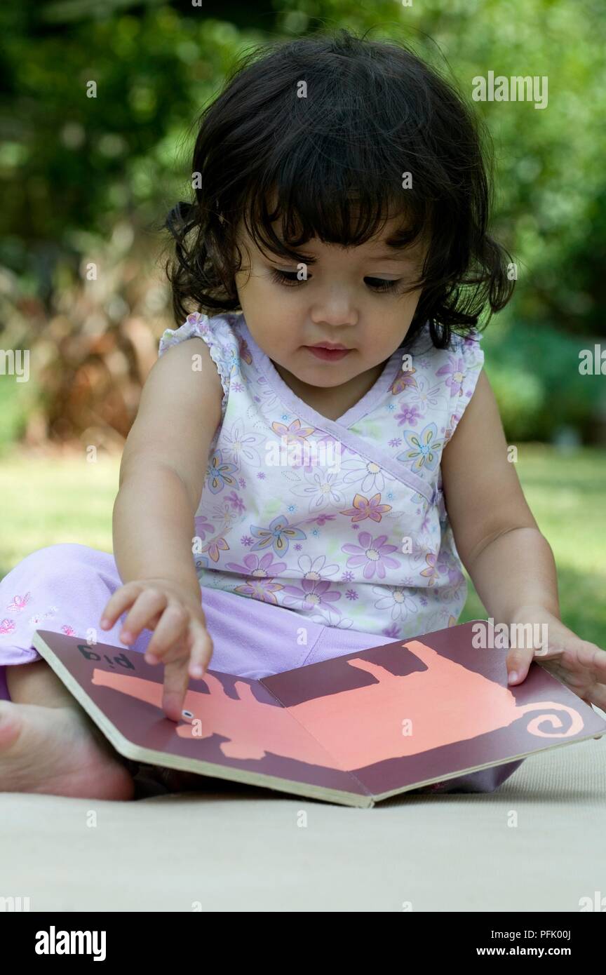 Dai capelli scuri bambina guardando picture book in giardino, close-up Foto Stock