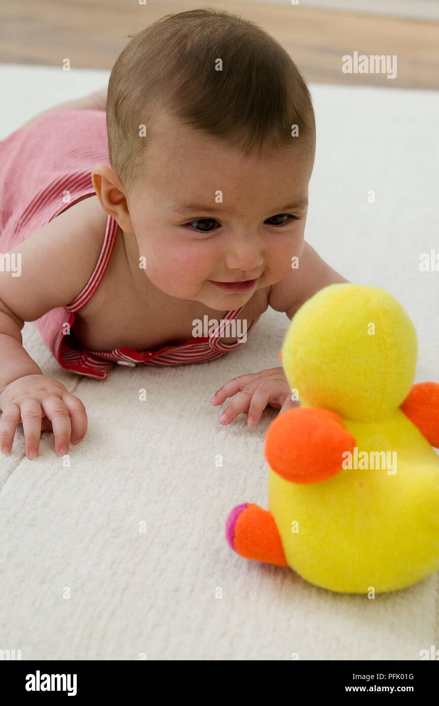 Baby girl guardando toy duck, sorridente, close-up Foto Stock