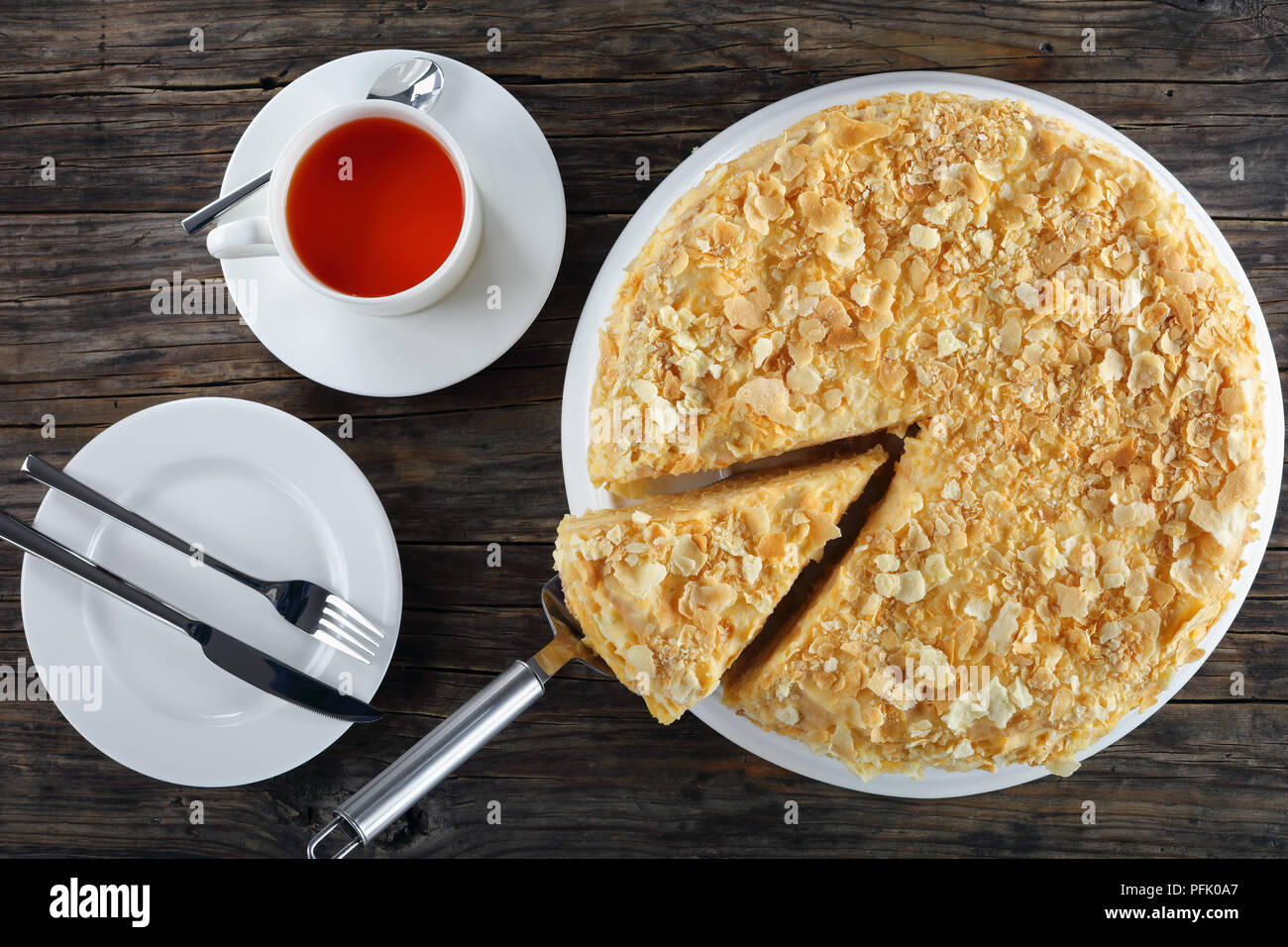 Deliziosa casa pasta sfoglia torta Napoleone stratificata con crema pasticcera sulla piastra bianca con un pezzo su una torta pala, vista da sopra, close-up Foto Stock
