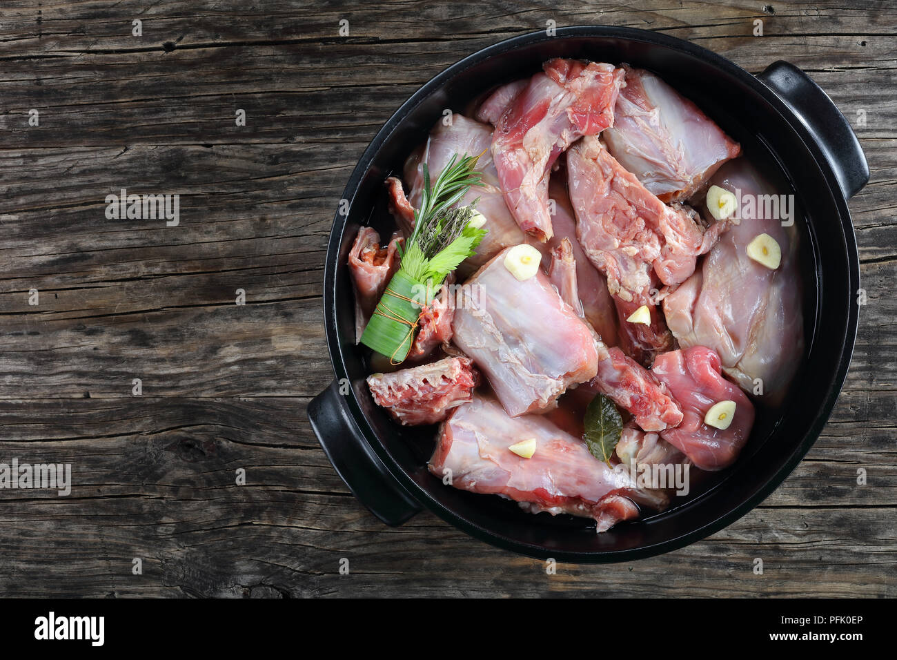 Pezzi di coniglio crudo marinato con vino bianco, aglio e spezie e il mazzetto di erbe aromatiche o bouquet garni in nero teglia, vista da sopra Foto Stock