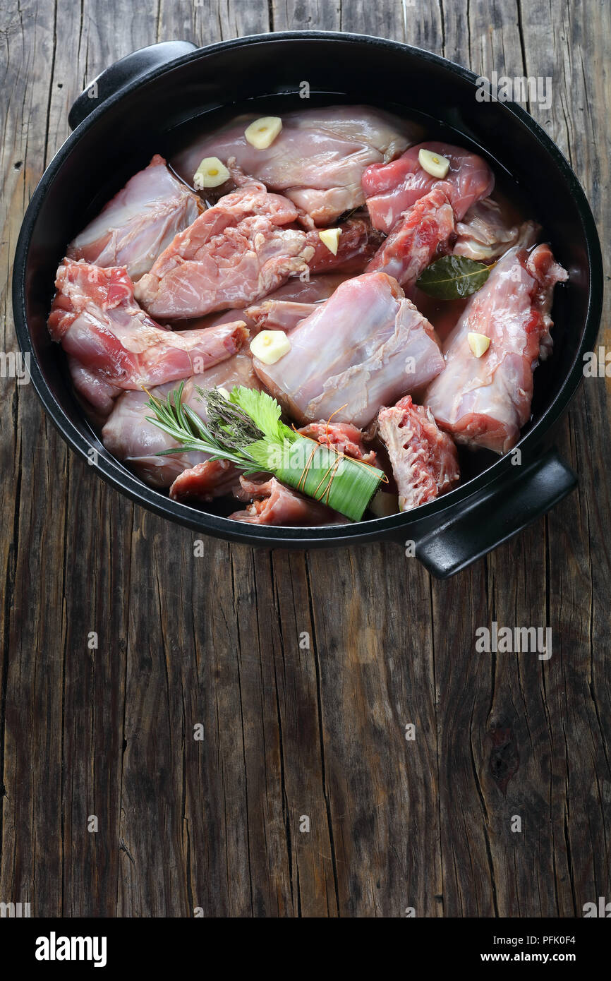 Pezzi di coniglio crudo marinato con vino bianco, aglio e spezie e il mazzetto di erbe aromatiche o bouquet garni in nero teglia, vista verticale da un Foto Stock