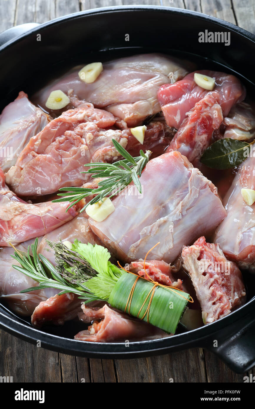 Pezzi di coniglio crudo marinato con vino bianco, aglio e spezie e il mazzetto di erbe aromatiche o bouquet garni in una teglia sul vecchio dark di tavole di legno, Foto Stock
