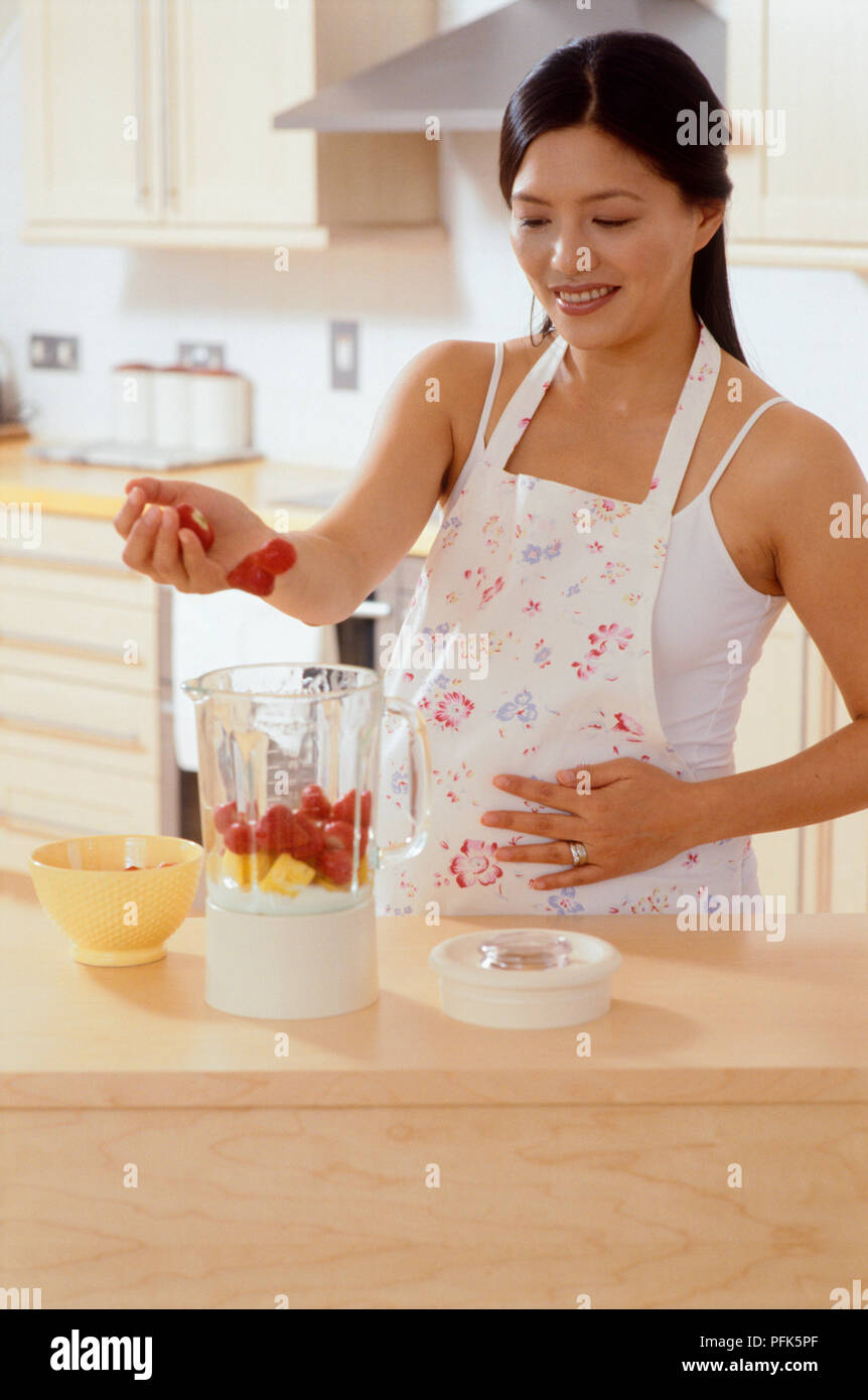 La donna in cucina frutta aggiunta al miscelatore Foto Stock