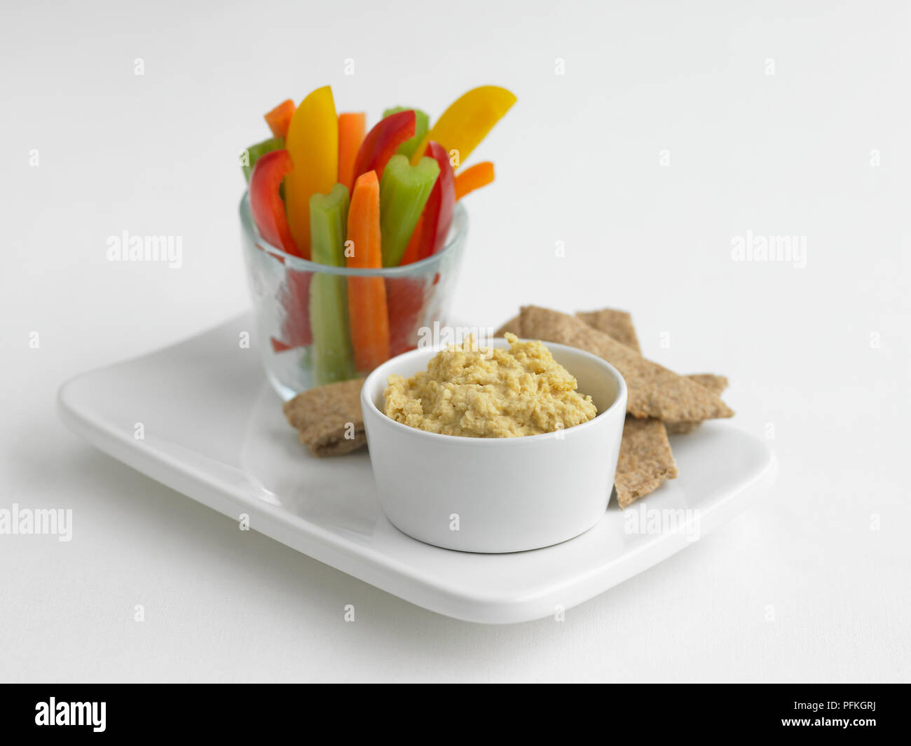 Ciotola di hummus, bastoncini di peperoni, la carota e il sedano in vetro, con pane pitta sul vassoio Foto Stock