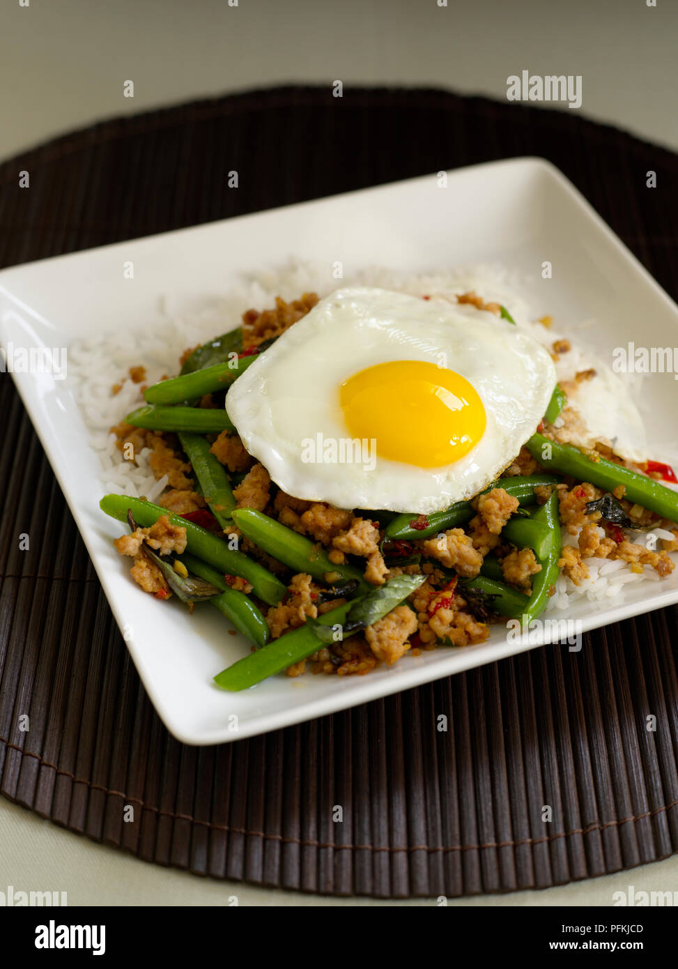 Pad kaprao gai, stir-fritto di pollo piccante con fagiolini, basilico tailandese e guarnita con uovo fritto Foto Stock