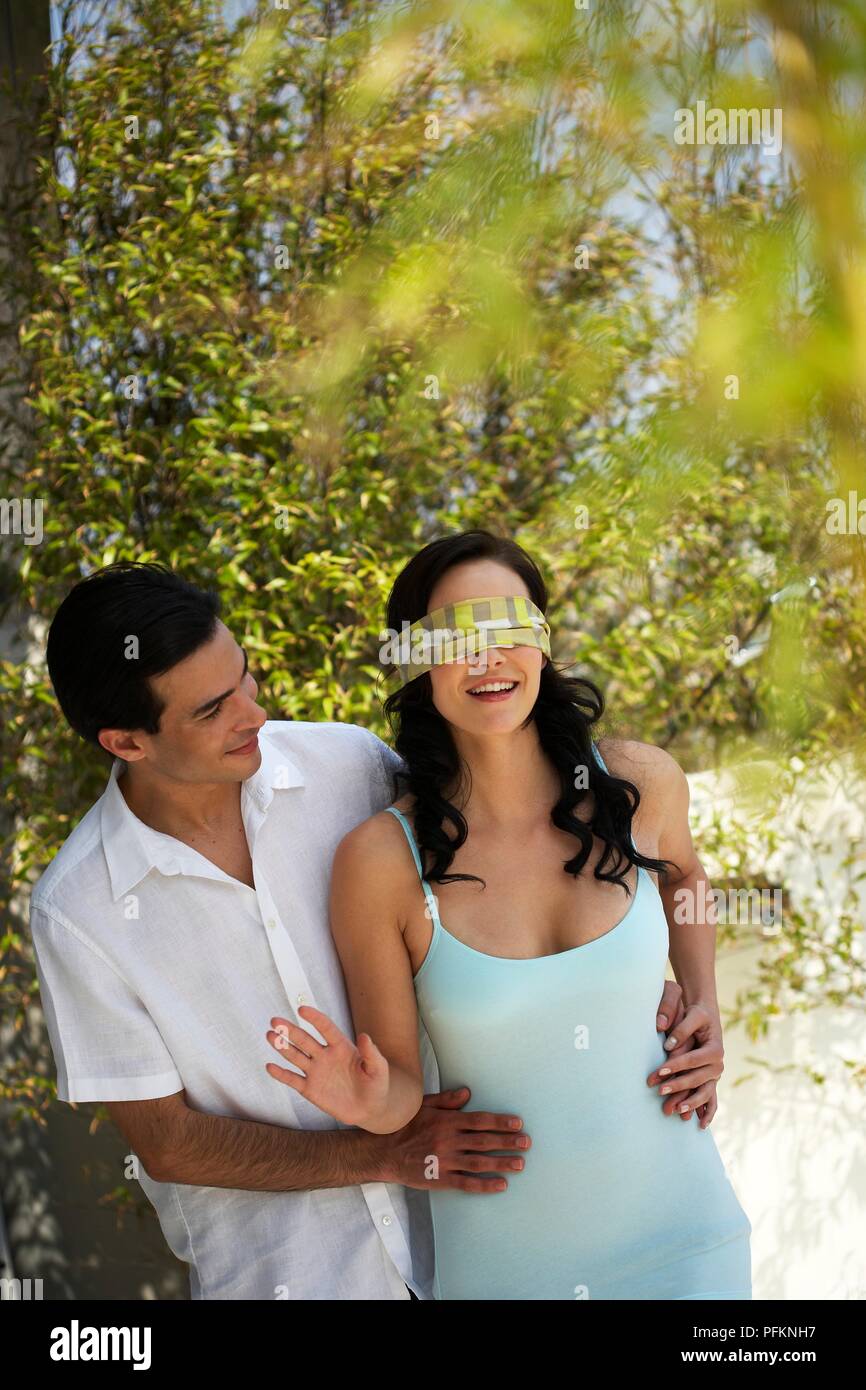 Uomo con le braccia intorno a occhi bendati donna in abiti estivi Foto Stock