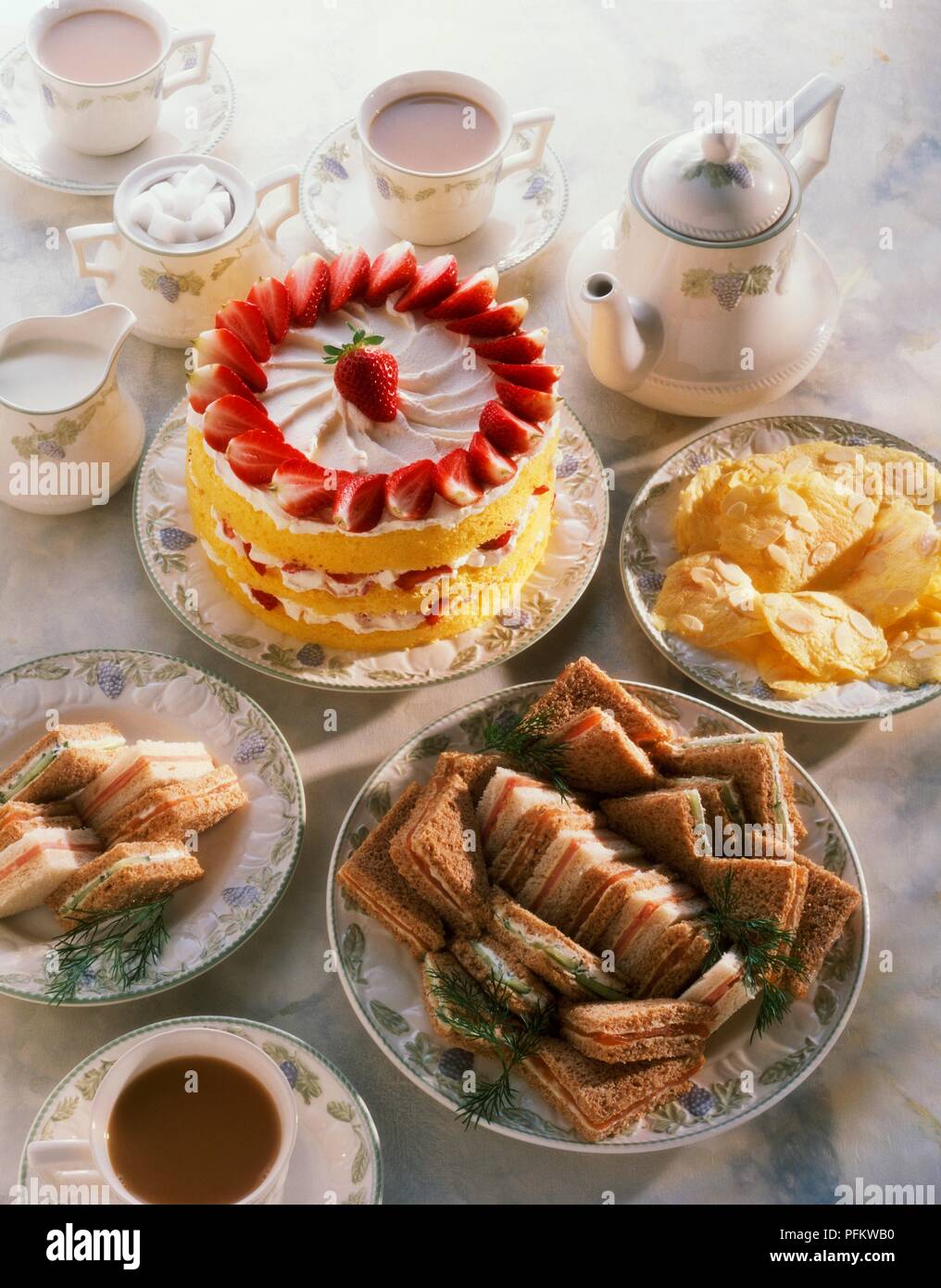 La tabella di cui alla fragola pan di spagna, club sandwich, biscotti, teiera e tazze di tè Foto Stock