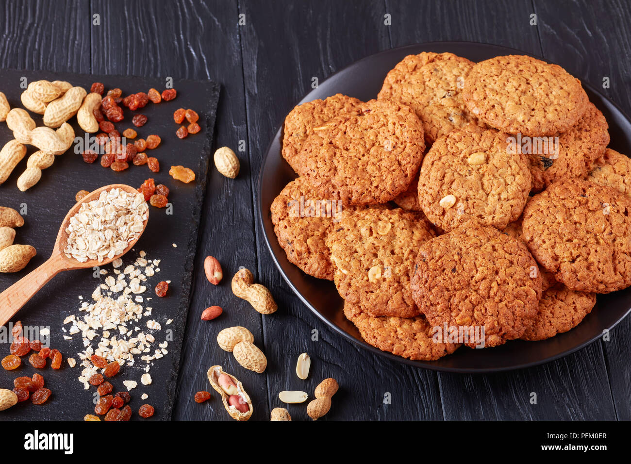 Lo zucchero di canna fiocchi d'avena, uva passa e arachide cookie su una piastra nera con ingredienti su un vassoio di ardesia, vista da sopra, close-up Foto Stock