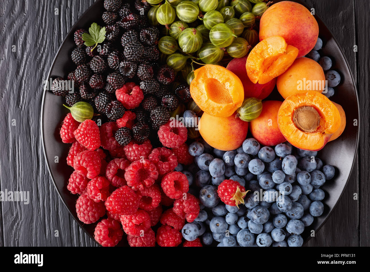 Close-up di frutti e bacche insalata di organico fresco Ribes rosso e nero lampone, mirtillo, fettine di albicocche su una piastra nera su una tavola di legno Foto Stock
