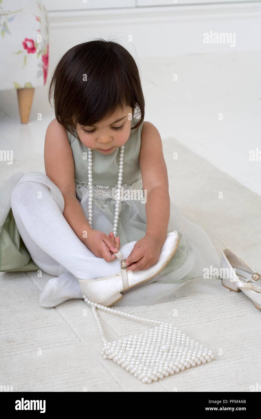 Ragazza che indossa collana di perle seduto a terra il fissaggio scarpe da ballo Foto Stock