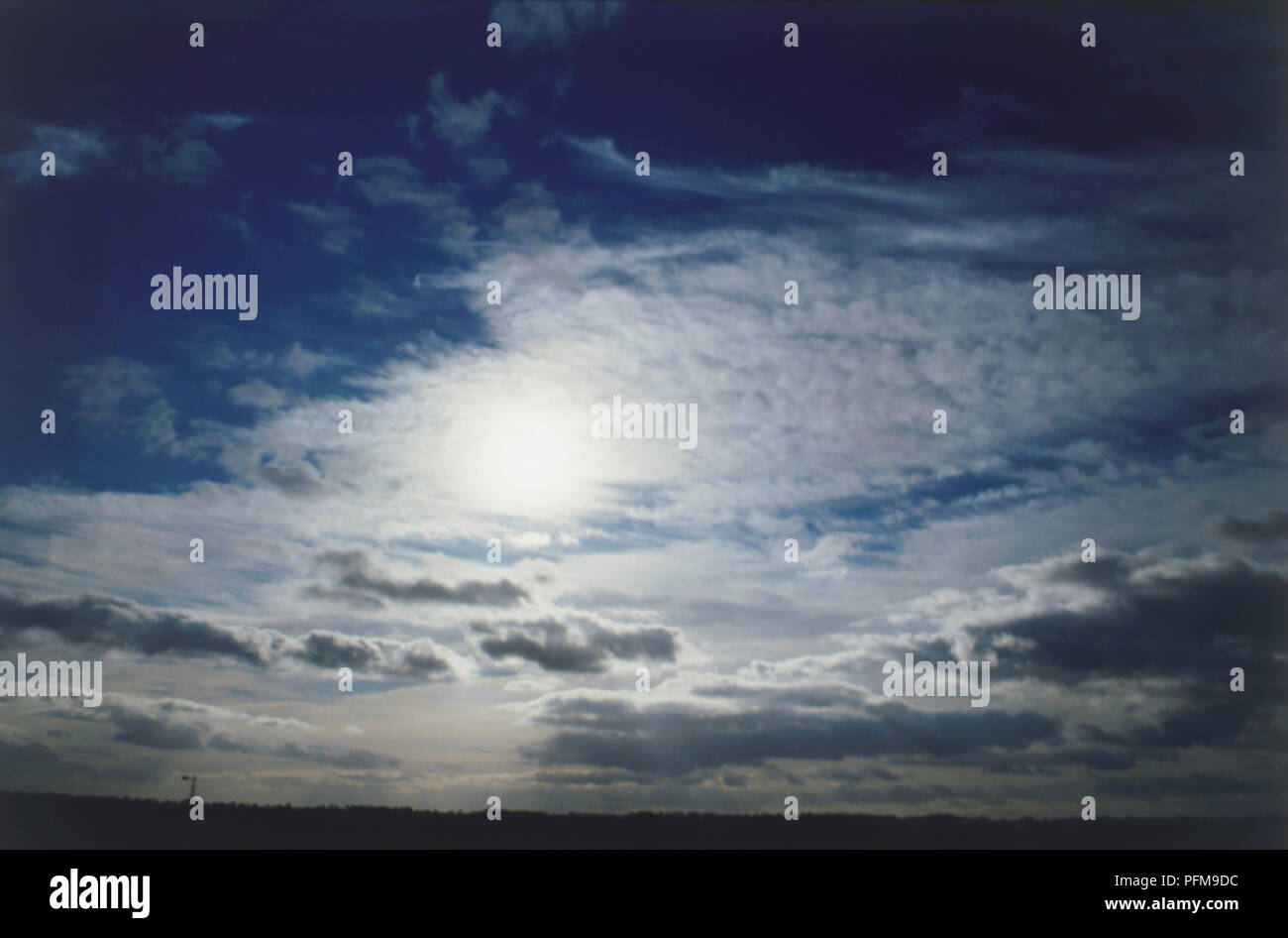 Cirrocumulus con Stratocumulus in un oscuramento del cielo al fondo ma con il sole che splende dietro le nuvole nella parte superiore dell'immagine. Foto Stock