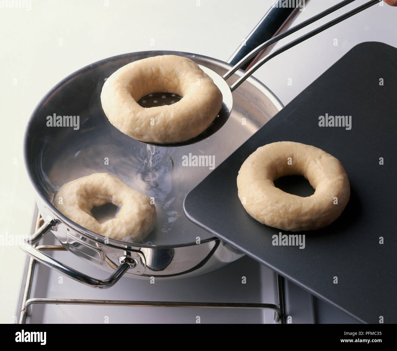 Close-up di bagel ebollizione in una pentola, una essendo sollevato fuori con la schiumarola e un altro sul vassoio da forno nelle vicinanze, close-up Foto Stock