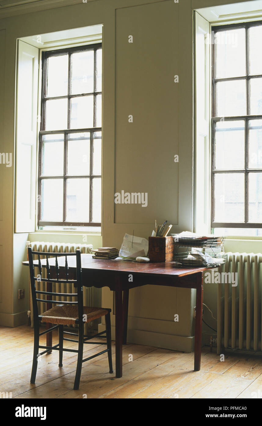 Tavolo di lavoro davanti a due finestre a ghigliottina con radiatori sotto le finestre e pavimento in legno. Foto Stock