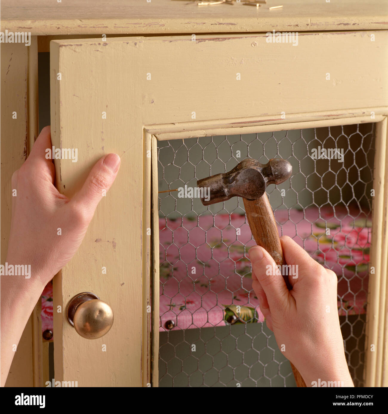 Martellatura mani vecchia credenza, fissaggio filo di pollo all'interno della porta della cucina. Foto Stock